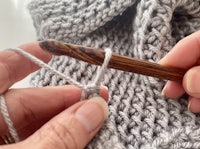 a person knitting a sweater with a wooden crochet hook