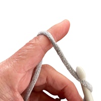 a person's hand holding a white crochet hook