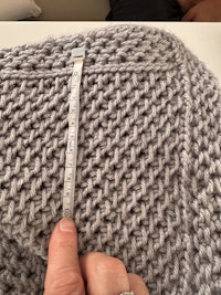 a person holding a measuring tape while knitting a grey sweater