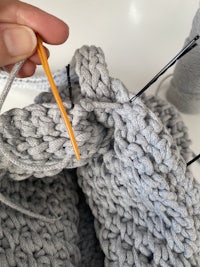 a person knitting a grey knitted bag with a needle