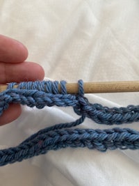 a person holding a knitting needle with a blue yarn