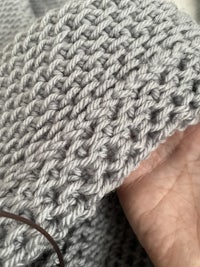 a person knitting a grey sweater with a needle