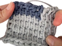 a pair of hands holding a grey and blue crochet stitch