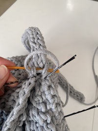 a person is knitting a grey sweater with a needle