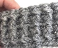 a person is holding a grey crocheted beanie