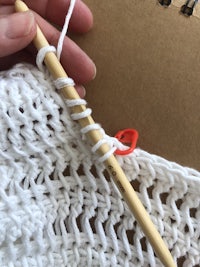 a person holding a crochet hook while knitting a white sweater