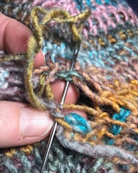 a person knitting a sweater with a needle