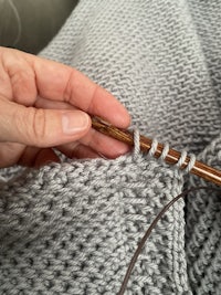 a person knitting a grey sweater with a wooden needle